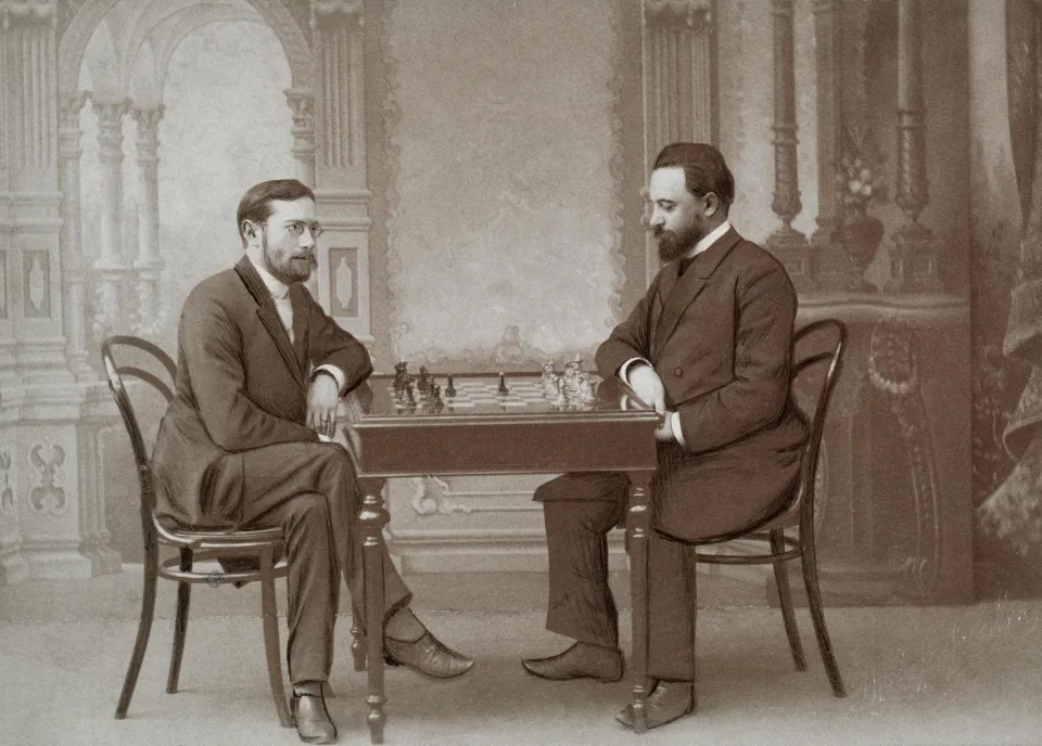 Ο Siegbert Tarrasch και ο Mikhail Chigorin καθισμένοι απέναντι σε σκακιέρα